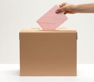Hand dropping an envelope into a feedback box, representing anonymous reporting channels at work.